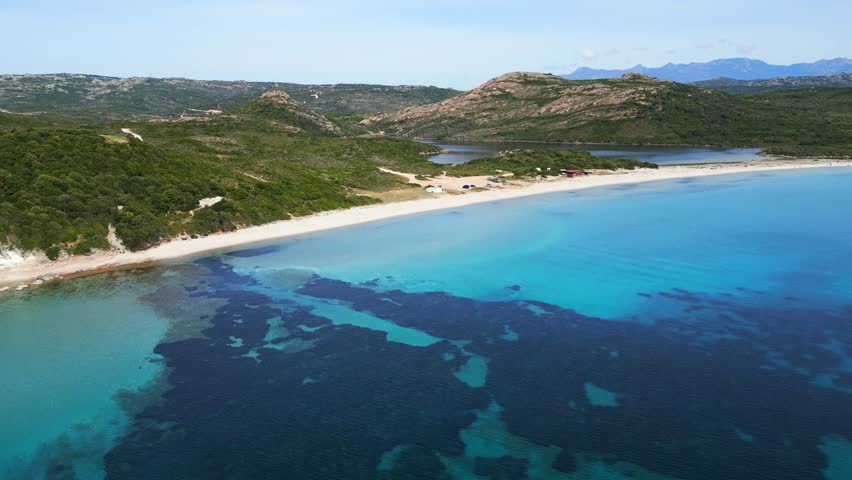 Aerial view over the translucent Mediterranean sea flying towards the deserted sandy beach of Plage de Balistra on the island of Corsica