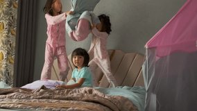 Family pillow fight with three asian girls in pajamas on bed in bedroom. - Powered by Shutterstock - Get 15% off with code: PIKWIZARD15