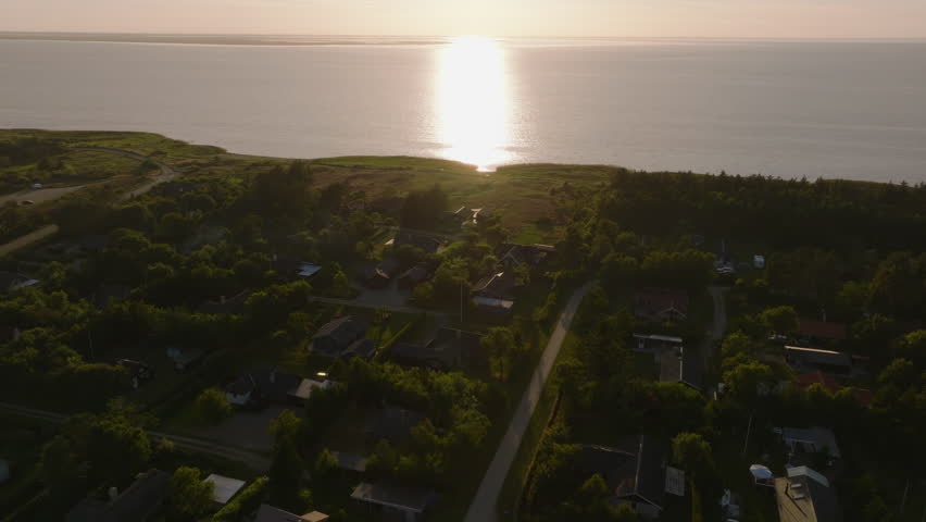 Aerial views capture sunlight shimmering on North Sea, showcasing a charming coastal town in Denmark during a serene summer evening