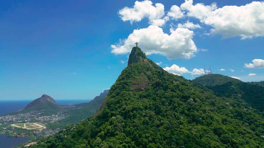 Aerial view of the Christ the Redeemer statue on Corcovado Mountain in Rio de Janeiro, Brazil, under a bright blue sky with scattered clouds.