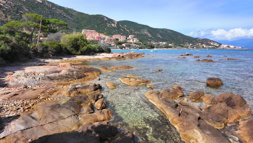 Rocky shoreline with scattered boulders near coastal village, Marinella Beach, Corsica.