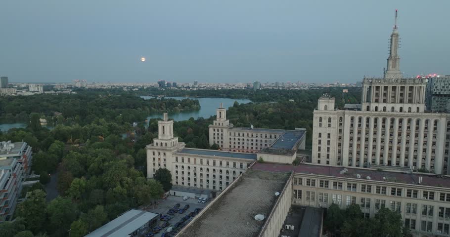 Aeriel View of the Casa Presei in Bucharest Romania at dusk with full moon rising and city skyline. Brutalist Soviet architecture and abandoned building in 4K.