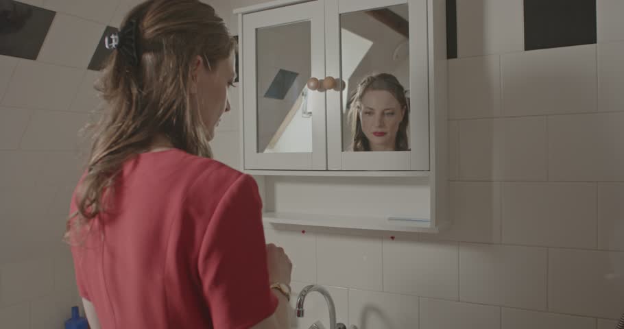 Zoom in of a woman dressed in a red dress taking off her wedding ring and leaving it in a white bathroom