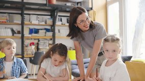 Elementary school children in an art lesson, drawing and coloring with pencils and crayons, and their modern teacher in glasses accompanies them in the creative process. one student eats a cookie - Powered by Shutterstock - Get 15% off with code: PIKWIZARD15
