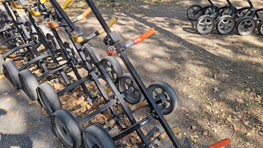 Line of black and orange push carts at a park during sunny autumn afternoon, ready for visitors to use