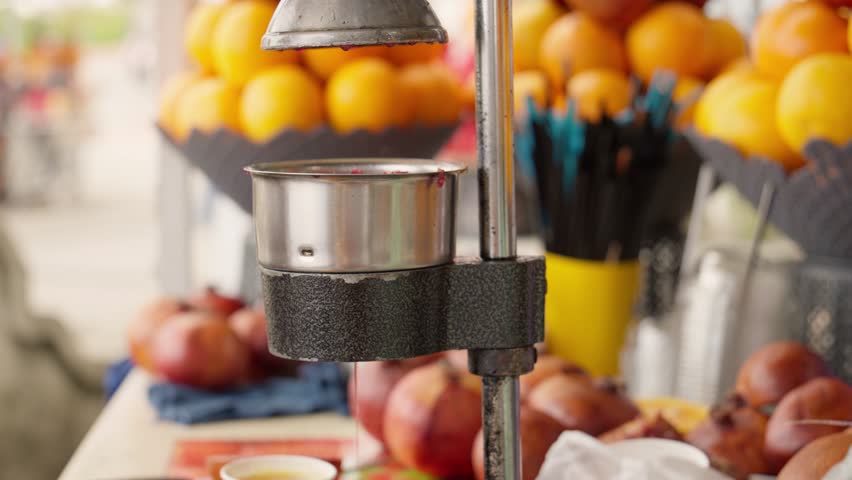 Street vendor wearing gloves prepares fresh pomegranate juice using manual fruit press, showcasing traditional method of extracting juice from ripe pomegranates in bustling market