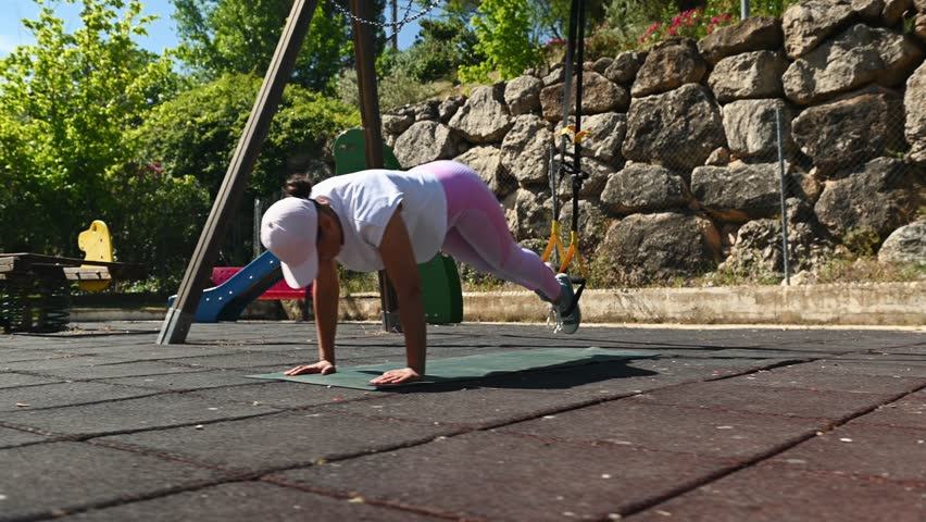 Outdoor workout with female athlete performing suspension training exercises in sunny park setting for fitness and strength