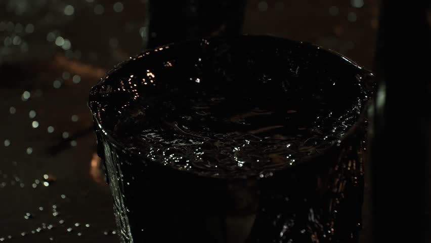 A worker collects fuel oil from the floor of an oil tank and pours it into a bucket close-up. Cleaning a tank of oil residues