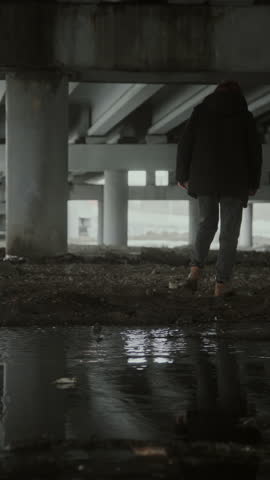 Vertical slow motion shot of hysterical young man picking up stone and throwing it into puddle in front of him, then leaving