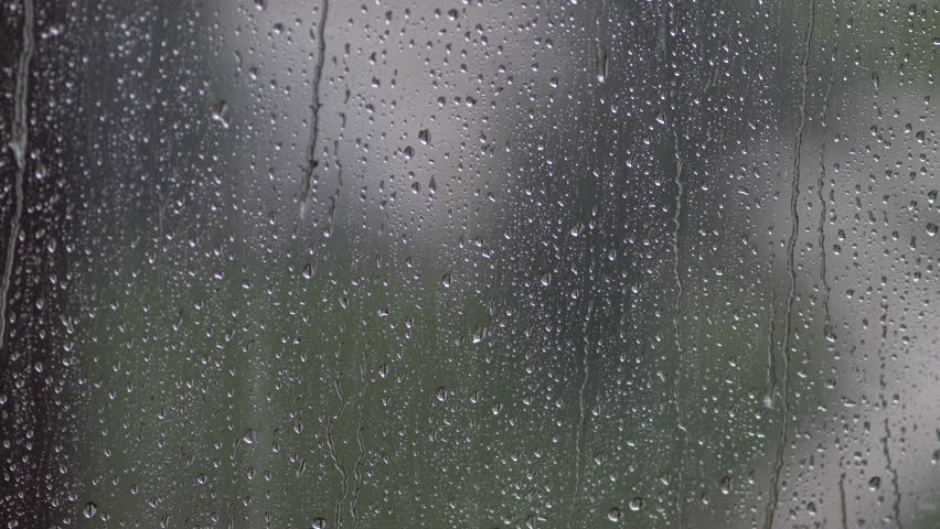 Rain droplets slide down windowpane, sunlight glimmers faintly outside. Overcast weather, feeling down, time to stay indoors at home, soft focus, selective focus