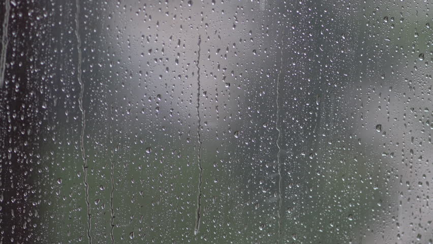 Rain droplets slide down windowpane, sunlight glimmers faintly outside. Overcast weather, feeling down, time to stay indoors at home, soft focus, selective focus