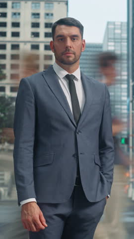 Vertical Screen: Caucasian Businessman in a Gray Suit Standing in the Middle of a City Intersection with Blurred Pedestrians Rushing By in a Timelapse Footage. Portrait of a Male Posing for Camera