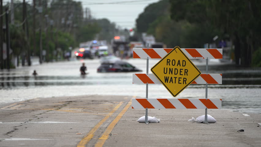 Flooded street in Florida after hurricane rainfall with road closed signs blocking driving of cars. Safety of transportation during natural disaster concept