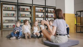 A teacher sits with her back to the camera, telling a story to her elementary students as they listen attentively on the floor in a cozy, modern school library filled with books. - Powered by Shutterstock - Get 15% off with code: PIKWIZARD15
