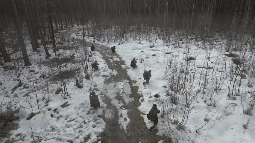Soldiers in Snow Covered Terrain Training for Cold Weather Military Maneuvers. Equipped military unit used in camouflage on military reconnaissance missions. Rifle in shooting position in dense forest