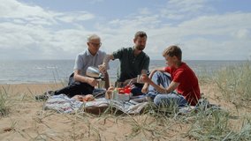 Boy, father and grandfather relaxing on beach having picnic on blanket. Grandson, adult father and older man, sitting, chatting and enjoying buns and tea from thermos. Male generations togetherness - Powered by Shutterstock - Get 15% off with code: PIKWIZARD15