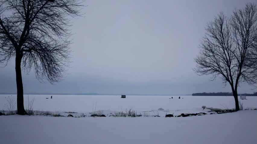 A group of ice fisherman near their ice shanty on a frozen lake. View from the snowy shore from between two trees. Shot on Lake Mendota, Madison, Wisconsin, Midwest USA.