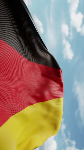 Wavy flag of Germany blowing in the wind in slow motion. Waving colorful German flag team symbol abstract vertical background. Blue sky with clouds. World countries flying flags concept