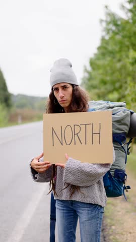 A woman is holding a sign that says North. The hitchhiker is wearing a gray hat and a gray sweater