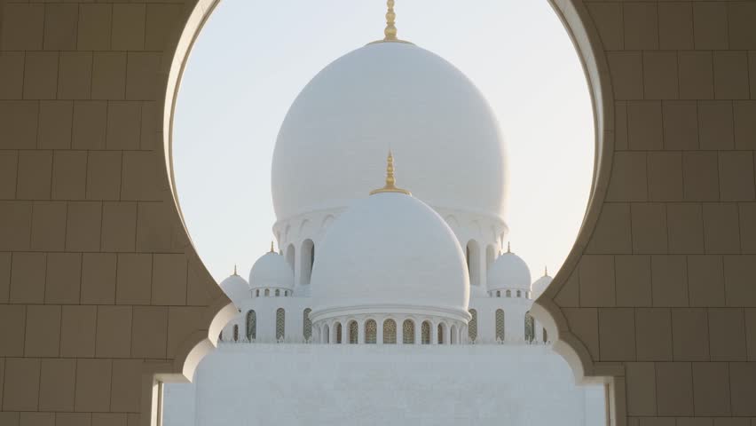 View of Domes of Sheikh Zayed Grand Mosque in Abu Dhabi, UAE framed by ornate arch. Islamic art and architecture. Popular Arabic place of worship and a landmark