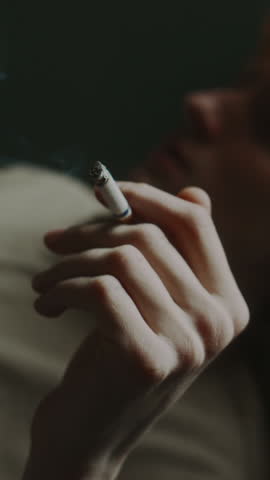Vertical close-up shot of melancholic young man smoking cigarette and reminiscing in horizontal position
