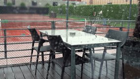 Outdoor patio furniture drenched from rain, viewed through a window with raindrops, against the backdrop of a wet and empty tennis court, creating a somber and deserted feel - Powered by Shutterstock - Get 15% off with code: PIKWIZARD15