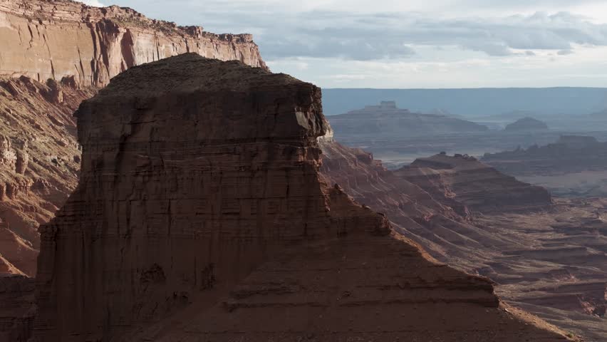 A 70mm high-flying orbital drone shot around a massive, isolated rock tower, slowly revealing the intensely contoured cliffs of Hurrah Pass, in the unique and extreme desert landscape of Moab, Utah.