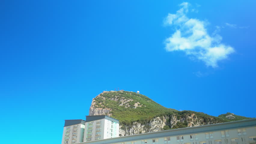 Scenic view of the iconic Rock of Gibraltar with residential buildings in the foreground, set against a vibrant, clear blue sky