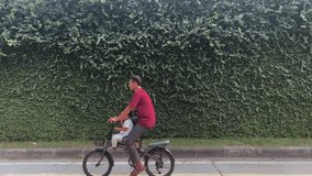 A man cycling passes in front of the camera. with a plant background on the wall - Powered by Shutterstock - Get 15% off with code: PIKWIZARD15