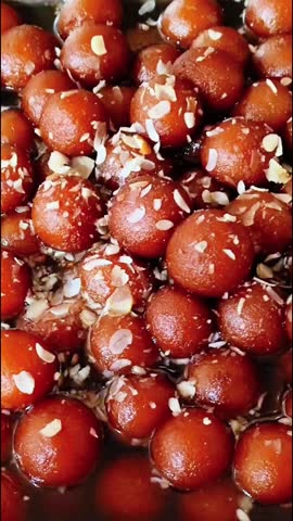 Gulab jamun, a ball shaped Indian sweet dumplings, heaped in a container with shreds of dry fruits, a top view close up video.