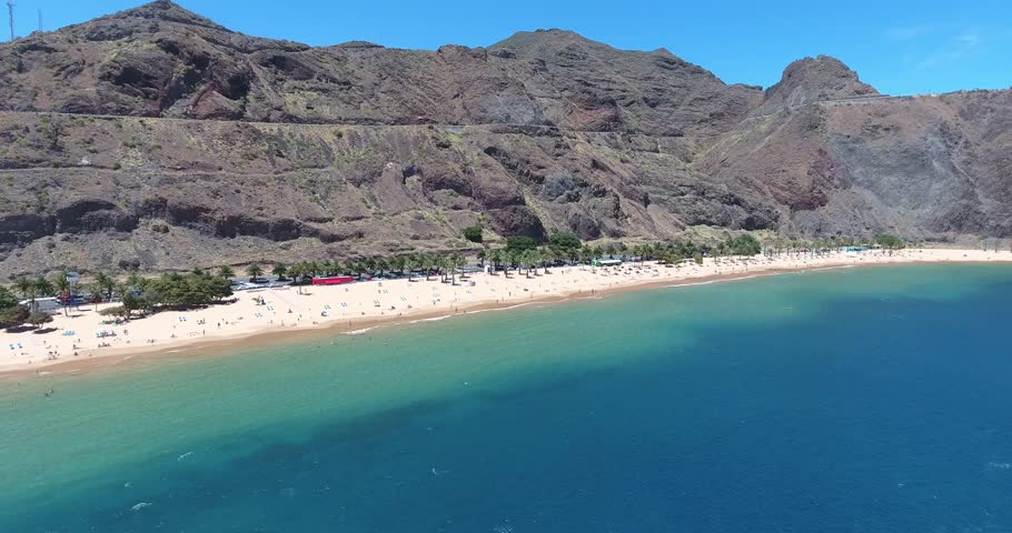 Aerial view of Playa de Las Teresitas, a famous golden sand beach near Santa Cruz de Tenerife, Canary Islands. Calm turquoise waters, palm trees, and stunning coastal scenery.

