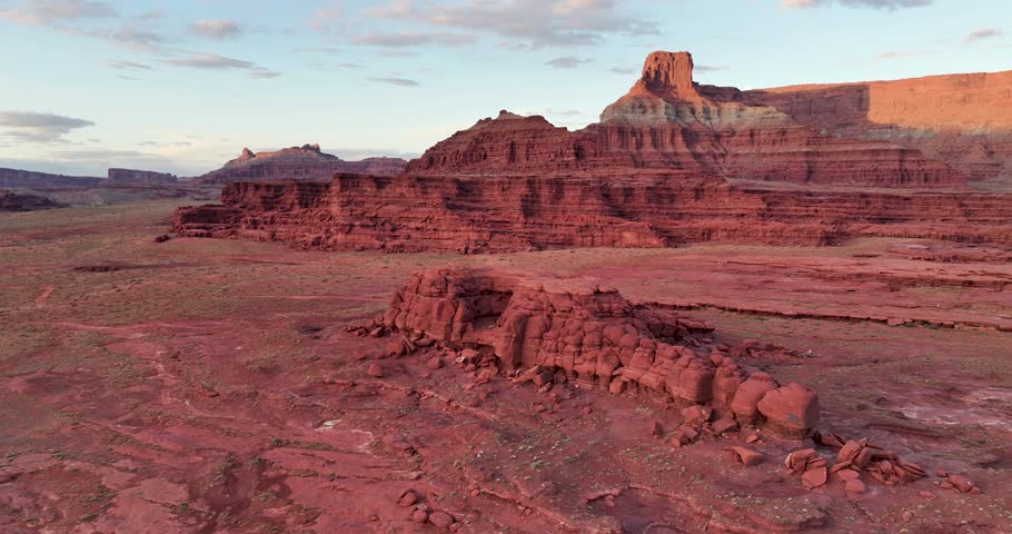 A high-flying orbital drone shot of the unique and extreme desert landscape of Moab, Utah. The camera rotates around the isolated Catacomb Rock, with intensely contoured cliffs in the distance.