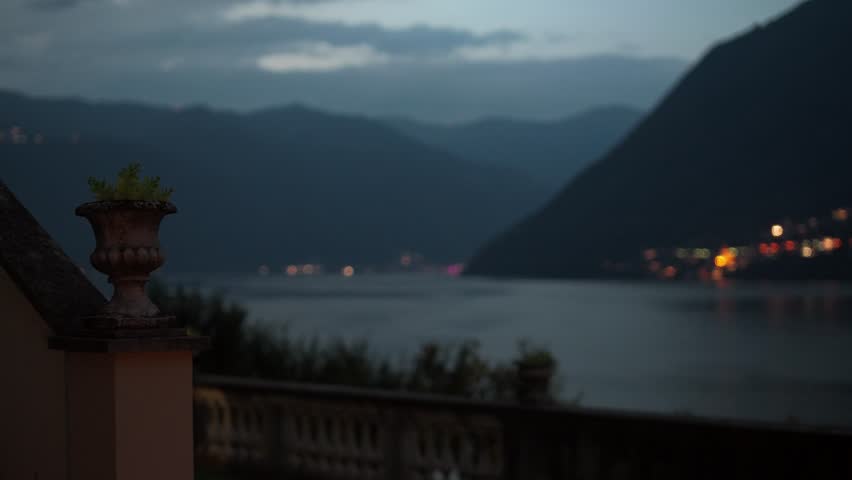 A balcony vista of Lake Como at dusk. The camera focus racks from the foreground plants to the scenery.
