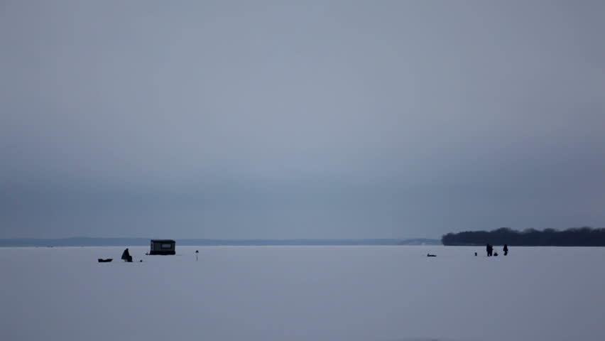A group of ice fisherman quietly standing and sitting near their ice shanty on a frozen lake. Shot on Lake Mendota, Madison, Wisconsin, Midwest USA.