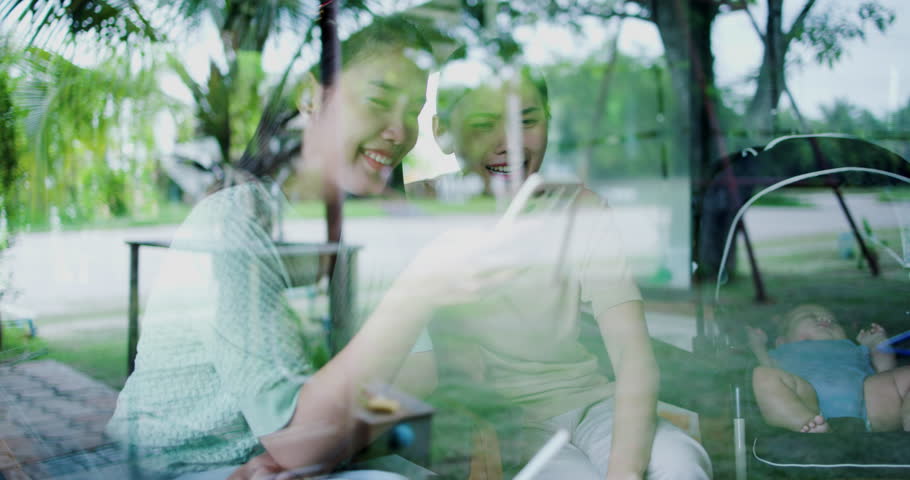 Handheld selective focus shot, Two happy siblings sit at a table playing social media together on smartphone while waiting for little boy to wake up. Family enjoying happy time together.