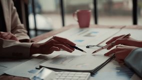Two businesswomen engage in a discussion about financial data, pointing at charts and graphs while using pens to emphasize key information - Powered by Shutterstock - Get 15% off with code: PIKWIZARD15