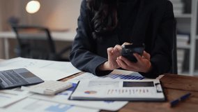 Businesswoman sitting at a desk analyzes financial data on a smartphone. Using a calculator, she reviews charts and graphs for insights and trends - Powered by Shutterstock - Get 15% off with code: PIKWIZARD15