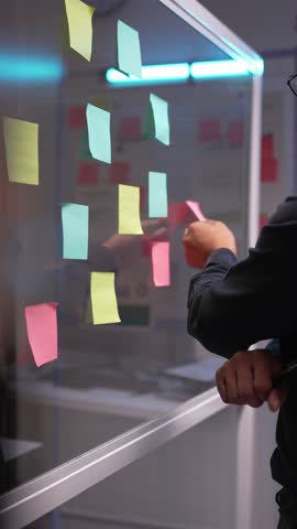 Colorful post it notes cover a glass wall in a modern office as a project manager organizes tasks. The vibrant notes boost creativity and enhance workflow efficiency
