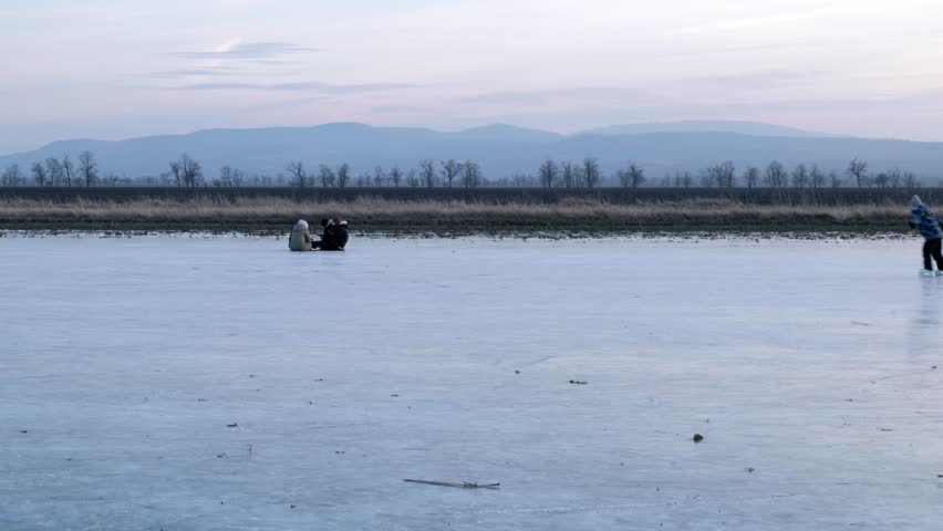 Children sledding on a frozen lake at dusk with mountains in the distance