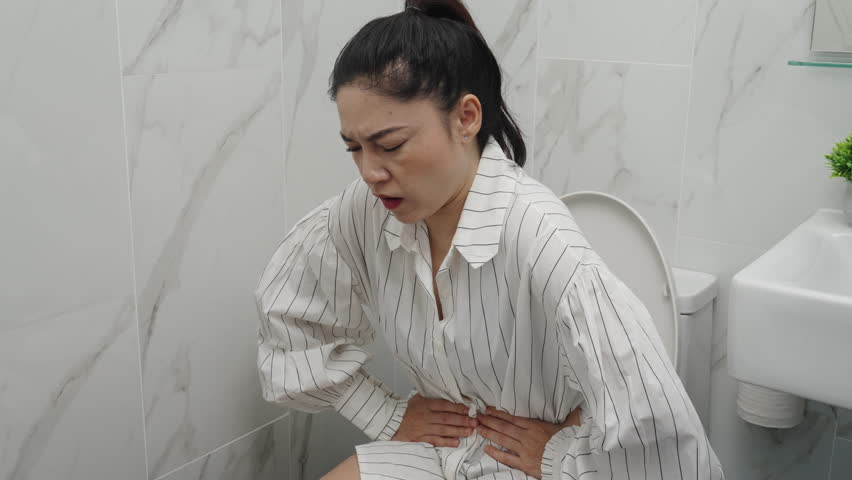 woman sitting on toilet bowl and holding her painful Stomach in the bathroom