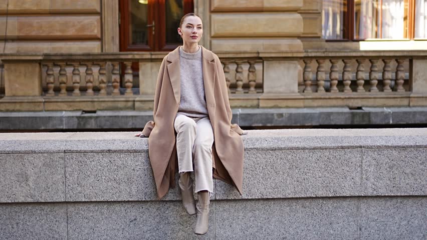 Young playful woman wearing coat sits and admires the city centre of Prague, Czech republic, Europe.