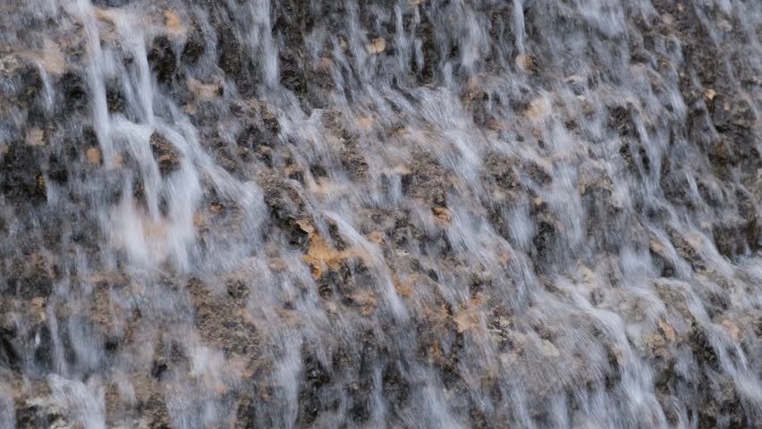 Waterfall close-up. The water flows down the steep stones. Camera movement from bottom to top. Natural abstract background. The concept of movement, calmness, balance. Grey autumn cloudy day