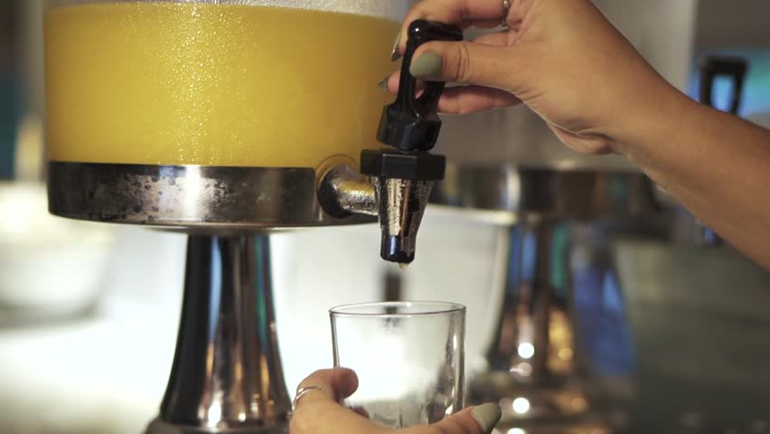 Closeup shot of hotel guest serving orange juice from dispenser at dining room during breakfast. Scene focused on dispenser. Blurred background. Shot on 1080p at 100fps.