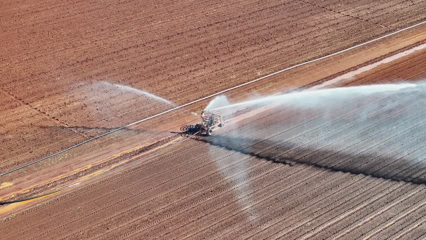 Farm irrigator watering ploughed red dirt paddock field, farming agriculture agricultural equipment, water use conservation environment