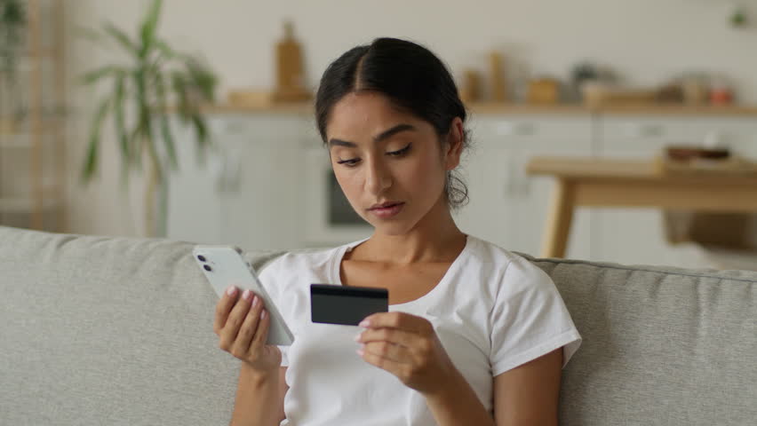 Confused worried Indian woman Arabian lady girl female problem mobile phone at home try buying purchase trouble online shopping credit reject blocked bank card internet app order food delivery failure