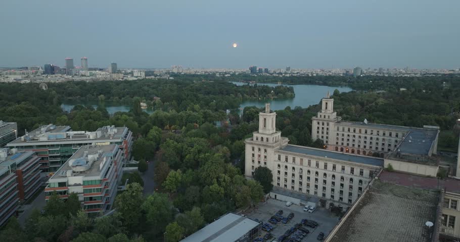 Aeriel View of the Casa Presei in Bucharest Romania at dusk with full moon rising and city skyline. Brutalist Soviet architecture and abandoned building in 4K.