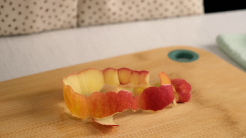Apple peel on wooden board on kitchen at home, woman peels apple. Female housewife in dress preparing dish from apples. Culinary, cuisine, healthy eating, baking concept.