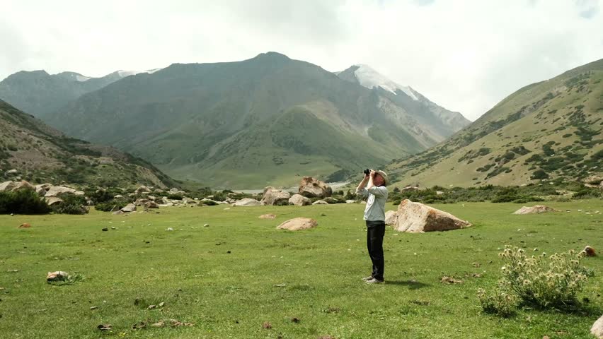 Adult man looking through binoculars in mountains in summer, nature observation
