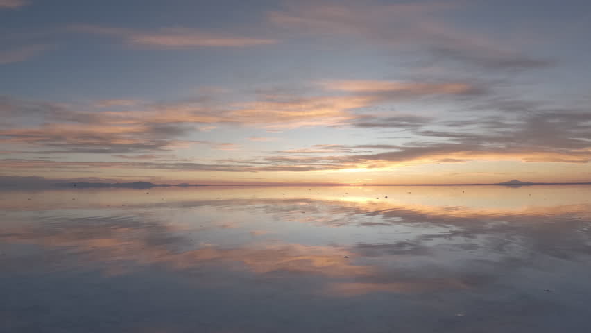 Timelapse during sunset in the salt flats in Bolivia South America with pink and orange sky reflecting in the mirror water on a sunny day with clouds and no people and a mountain in the background