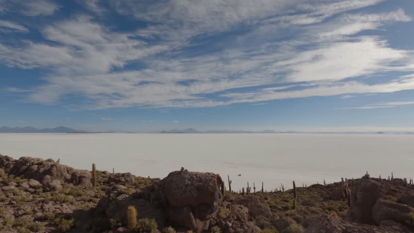 Timelapse filmed from cactus island in the middle of the salt flats in Bolivia on a sunny day with some clouds viewing over the wide landscape with cactus and rocks in the foreground